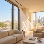 Luxury NYC penthouse interior with a floor-to-ceiling window cracked open, white curtains blowing in the spring breeze, and a view of the Manhattan skyline.