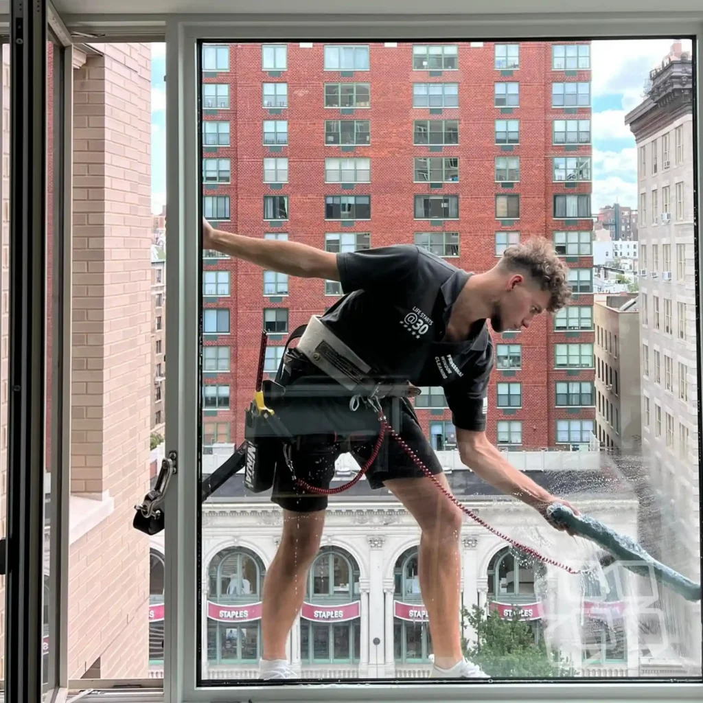Technician cleaning exterior window glass outside an occupied corporate building in New York