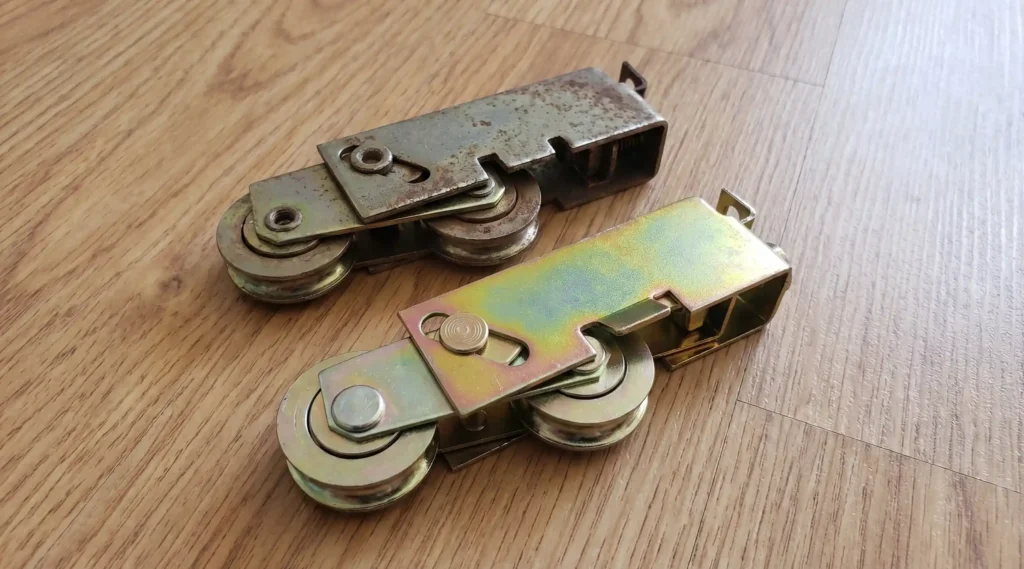Worn corroded sliding door roller wheels next to a new tandem roller assembly replacement