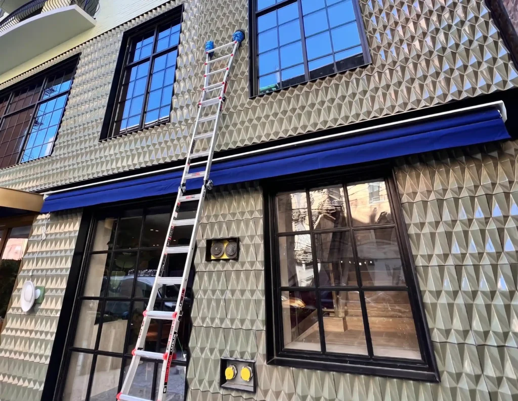 Extension ladder positioned against a boutique commercial facade with geometric textured tile cladding and black steel-frame windows in Manhattan