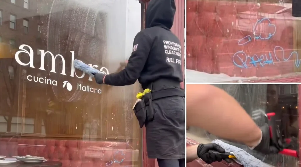 Window technician removing graffiti tags from an Italian restaurant storefront in New York City using a scrubber and razor scraper