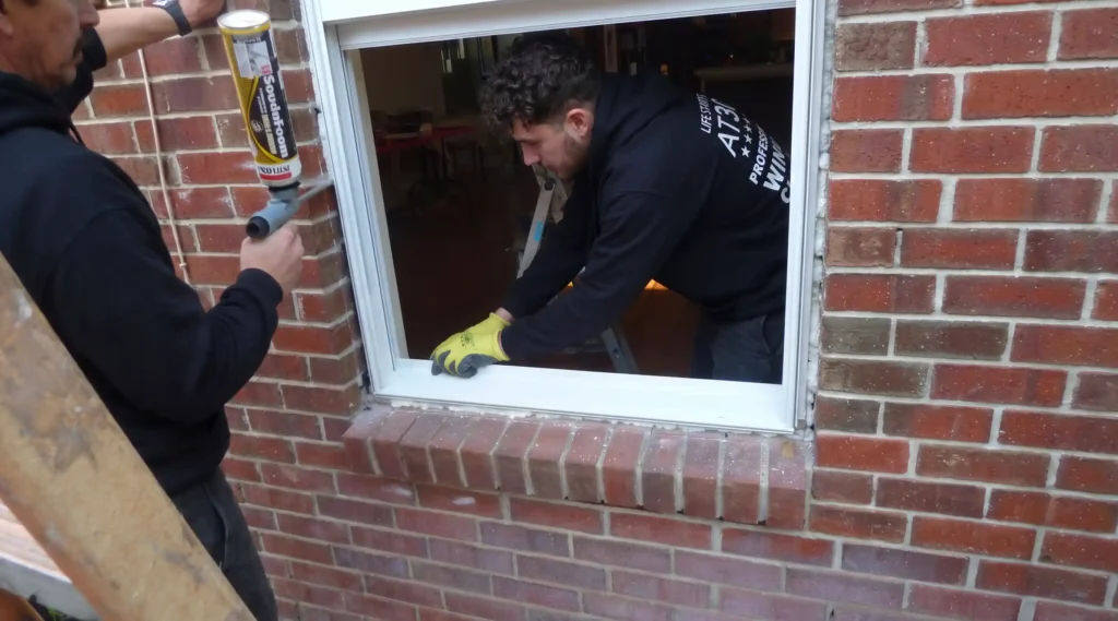 Big Apple Window Cleaning company technicians installing and sealing a replacement house window in a brick wall