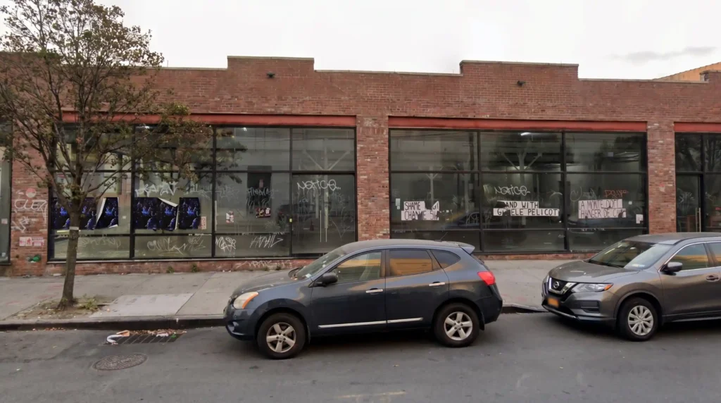 Commercial building storefront windows covered in graffiti tags and scratch vandalism on a Bushwick Brooklyn street