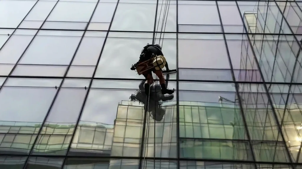 Rope access window cleaner descending a glass curtain wall skyscraper facade in New York City on a dual-rope system