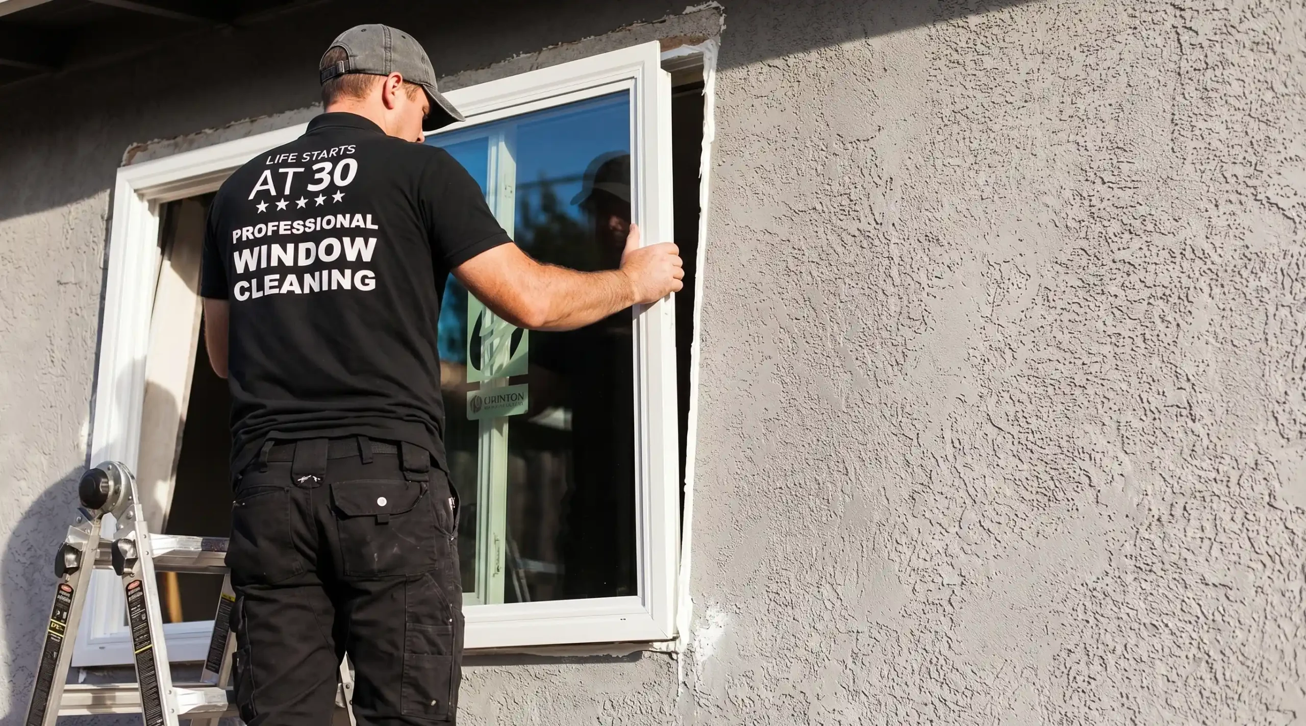 Window technician on a ladder removing a sliding window sash from a stucco exterior wall during replacement