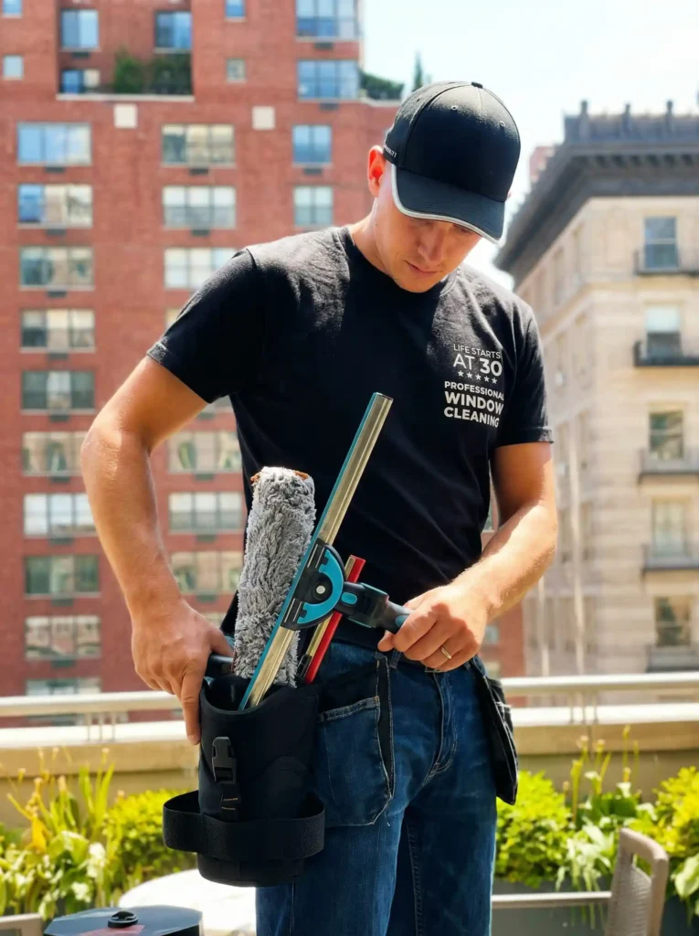 Professional window cleaner organizing tools in a BOAB holster on a New York City rooftop terrace with brick buildings behind