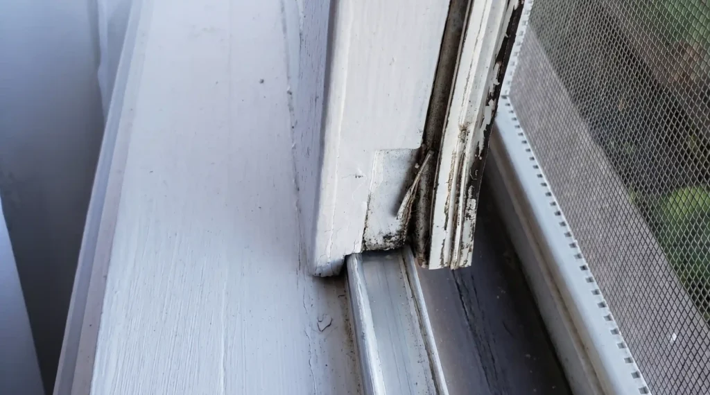 Severely deteriorated sliding window frame corner with rot, mold, and paint failure requiring full replacement
